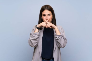 İzole edilmiş mavi duvarda genç bir kadın sessizlik işareti gösteriyor.