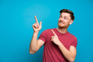 İşaret parmağı ile işaret izole mavi duvarda Redhead adam harika bir fikir