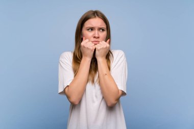 Mavi duvar üzerinde genç kadın biraz gergin ve ağzına eller koyarak korkuyor
