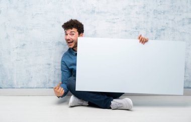 Genç adam bir kavram eklemek için boş bir beyaz pankart tutarak katta oturan