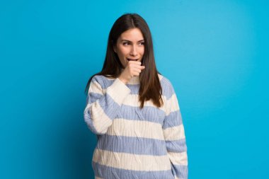 Mavi duvarın ardındaki genç kadın öksürük ve kötü hissetmekten acı çekiyor.