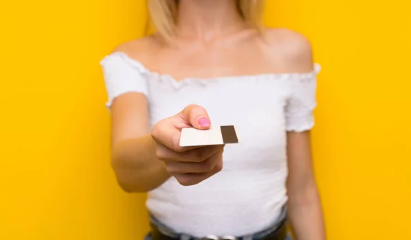 一个金发碧眼的年轻女子拿着信用卡翻过孤立的黄墙 — 图库照片