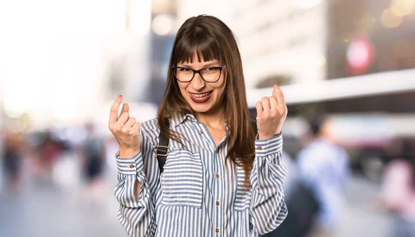 Woman with glasses making money gesture at outdoors