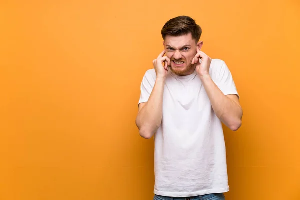 Redhead man over brown wall frustrated and covering ears