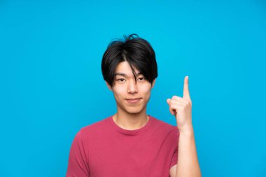 Işaret parmağı ile işaret izole mavi duvar üzerinde kırmızı gömlek ile Asyalı adam harika bir fikir