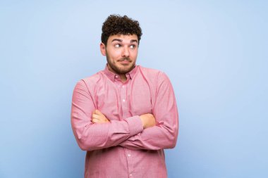 İzole mavi duvar üzerinde kıvırcık saçlı adam omuzları kaldırırken şüphe jest yapma