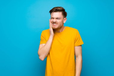 Diş ağrısı ile mavi duvar üzerinde Redhead adam