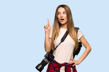 Genç fotoğrafçı kadın, izole edilmiş mavi arka planı işaret eden bir fikir düşünüyor.