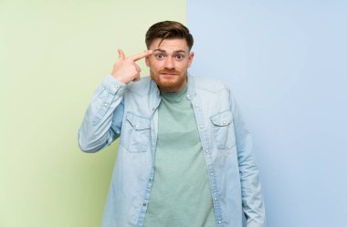 Kırmızı kafalı adam renkli arka plan üzerinde kafasına parmak koyarak delilik jest yapma