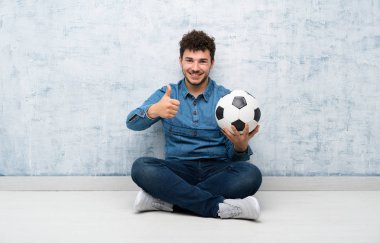 Yerde futbol topu tutan genç adam