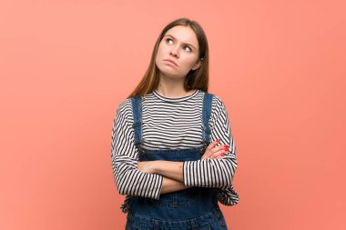 Pembe duvarda tulumlu genç bir kadın ciddi bir yüzle yukarı bakıyor.