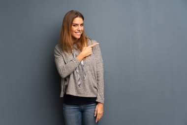 Sarışın kadın tarafına işaret gri arka plan üzerinde bir ürün sunmak için