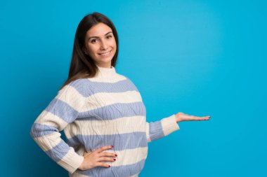 Mavi duvarın ardındaki genç kadın geriye bakıyor ve bir ürün sunuyor.