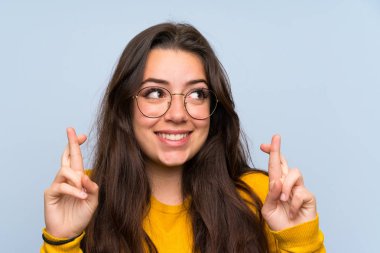 Parmakları geçerken izole mavi duvar üzerinde Genç kız