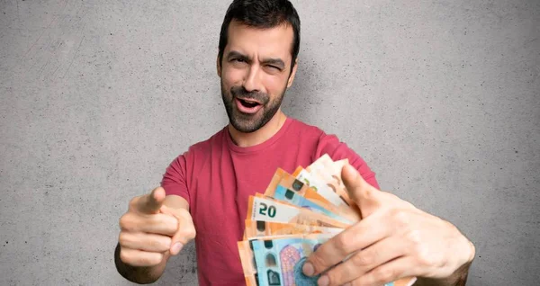 Man taking a lot of money points finger at you while smiling over textured wall