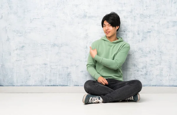 Asiatischer Mann Sitzt Auf Dem Boden Und Zeigt Nach Hinten — Stockfoto