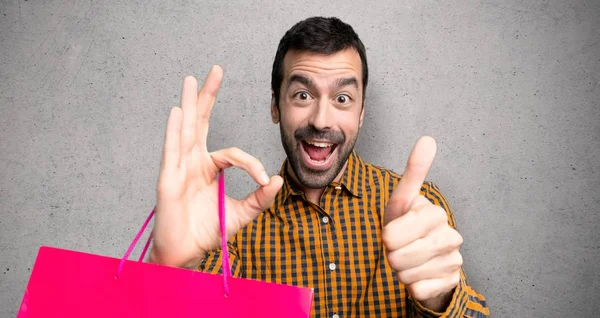 Man Shopping Bags Showing Sign Giving Thumb Gesture Textured Wall — Stock Photo, Image