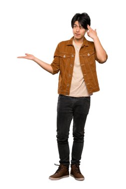 Kahverengi ceketli Asyalı bir adamın, izole beyaz arka planın üzerinde kafasına parmak koyarak delilik jesti yapan tam uzunlukta bir çekim