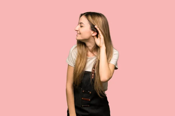 Mladá Žena Zástěrou Poslouchat Něco Tím Ruku Ucho Izolované Růžové — Stock fotografie