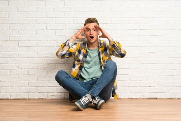 Blonde man sitting on the floor with surprise expression