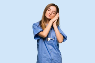 Genç hemşire, izole edilmiş mavi arka planda uyku jesti yapıyor.