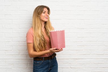 Beyaz tuğla duvarın üzerinde elinde patlamış mısır kasesi tutan genç sarışın kadın.