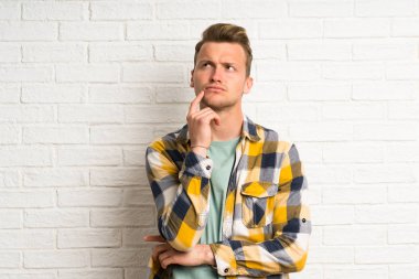 Beyaz tuğla duvar üzerinde sarışın yakışıklı adam şüpheleri olan ve yüz ifadesi karıştırmayın