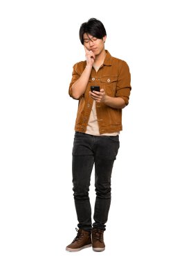 Kahverengi ceketli Asyalı bir adamın tam uzunlukta çekilmiş bir fotoğrafı, izole edilmiş beyaz arka plan üzerinden mesaj göndererek.