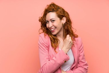 İzole pembe duvar üzerinde takım elbiseredhead kadın bir zafer kutluyor