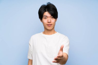 Iyi bir anlaşma dan sonra izole mavi arka plan handshake Asyalı adam