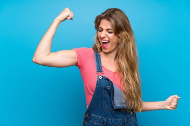 Önlüklü, mavi duvarlı genç sarışın kadın zaferi kutluyor.