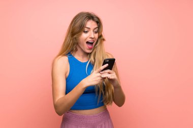 Soyutlanmış pembe arka planı olan genç sarışın kadın şaşırdı ve bir mesaj gönderiyor.