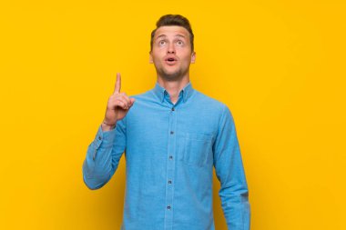 Sarışın adam izole sarı duvar üzerinde işaret ve şaşırttı