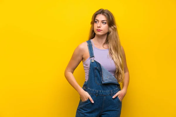 Jonge Blonde Vrouw Met Overalls Geïsoleerde Gele Achtergrond Staan Kijken — Stockfoto