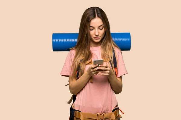 年轻的背包客女人在孤立的黄色背景上用手机传递信息 — 图库照片