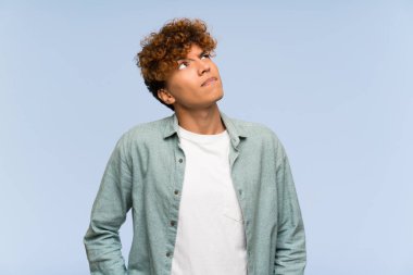 İzole edilmiş mavi duvarın üzerinde kafası karışmış genç Afro-Amerikan bir adam.