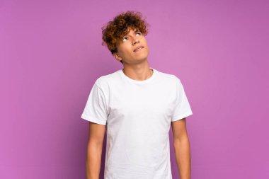 Genç Afro-Amerikan adam, yalıtılmış mor duvarın üzerinde, kafası karışık bir yüz ifadesiyle.