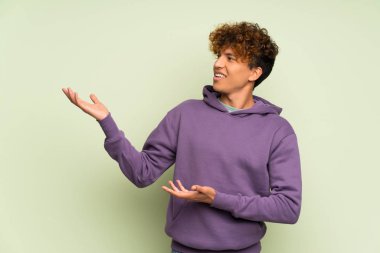 İzole edilmiş yeşil duvarın üzerinden elini uzatan genç Afrikalı Amerikalı adam.