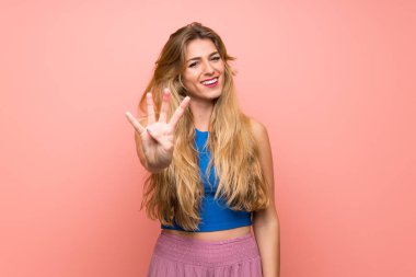 Soyutlanmış pembe arka planı olan genç sarışın kadın mutlu ve parmakları olan dört kişi sayıyor.