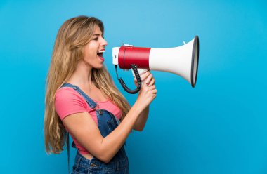 Tulumuyla mavi duvarın üstünde genç sarışın bir kadın megafondan bağırıyor.