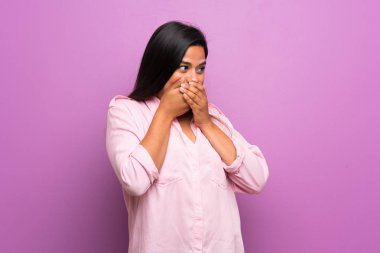 Genç Kolombiyalı kız mor duvarın üzerinden ağzını kapatıp yan tarafa bakıyor.