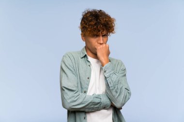 İzole edilmiş mavi duvarın üzerinde kuşkuları olan genç Afrikalı Amerikalı bir adam.