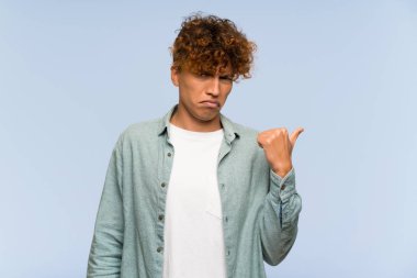 Genç Afro-Amerikan adam mavi duvarın üzerinde mutsuz ve kenarı işaret ediyor.