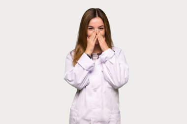 Gri arka planda ağzını kapatırken çok gülümseyen genç doktor kadın.