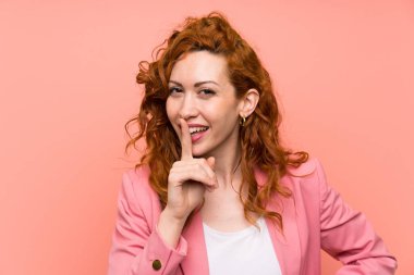 İzole pembe duvar üzerinde takım elbiseli Redhead kadın sessizlik jest yapıyor