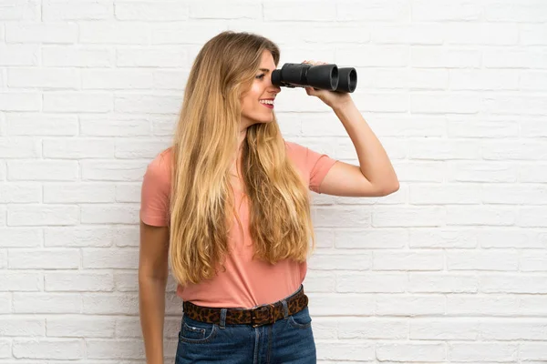 Mujer Rubia Joven Sobre Pared Ladrillo Blanco Con Prismáticos Negros —  Fotos de Stock