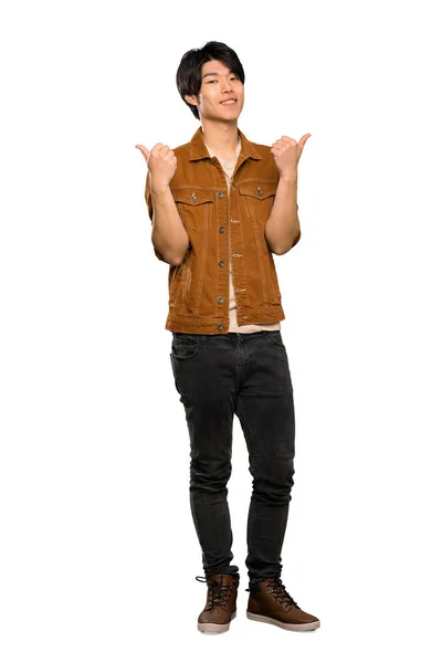 親指を上げたジェスチャーと孤立した白い背景の上に微笑む茶色のジャケットを持つアジア人男性のフルレングスショット — ストック写真