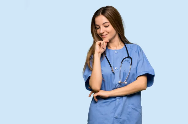 Jonge Verpleegster Kijkt Neer Met Hand Kin Geïsoleerde Blauwe Achtergrond — Stockfoto