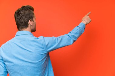 İşaret parmağı ile geri işaret izole duvar üzerinde Sarışın yakışıklı adam