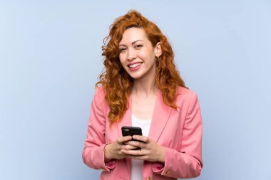 Izole mavi duvar üzerinde takım elbiseredhead kadın cep ile bir mesaj gönderme